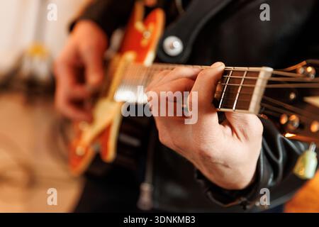 Aus der Nähe eines Musikers in einer Lederjacke, der Akkorde auf dem Griffbrett einer elektrischen Gitarre drückt. Stockfoto