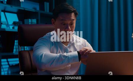 Workaholic Erwachsener asiatischer Geschäftsmann hart arbeitender Laptop Überprüfung Zeit mit Armbanduhr Deadline Problem japanischer Geschäftsmann Gefühl Stress Tippen Stockfoto