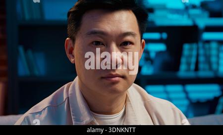 Portrait seriöser asiatischer ethnischer Mann mittleren Alters, der abends in die Kamera schaut dunkles Haus Wohnzimmer japanischer koreanischer Mann, der zuversichtlich in der Wohnung posiert Stockfoto