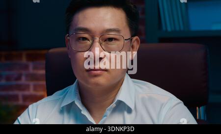 Portrait seriöser selbstbewusster asiatischer Geschäftsmann mittleren Alters in Brille Blick auf die Kamera posiert im Nachtbüro chinesischer Geschäftsmann koreanischer Mann Stockfoto