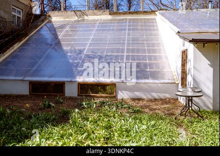 Solarpaneele, die auf dem schrägen Dach eines weißen Gebäudes in der Nähe eines Gartens installiert sind. Konzept für grüne Energielösungen, nachhaltigen Lebensstil und moderne Öko- Stockfoto