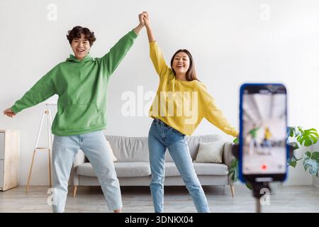 Glückliches junges asiatisches Paar, das Video auf dem Handy macht und zu Hause vor der Kamera tanzt Stockfoto