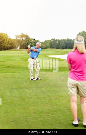 Senior Mann, Swing und Frau auf Golfplatz im Ruhestand mit Platz, Ziel und Bindung im Sommer. Leute, Paare und Golfer mit Sportausrüstung, Schuss oder Stockfoto