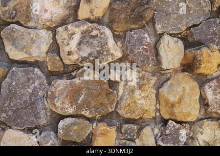 Steine in verschiedenen Größen und Farben bilden eine Wand. Die Steine sind eng aneinander angeordnet und zeigen verschiedene Texturen und Muster. Natürliches Licht Highli Stockfoto
