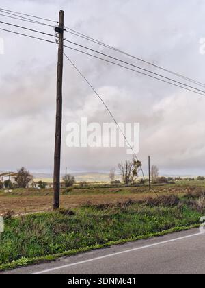 Aus der Vogelperspektive des verwitterten Holzpfahls mit Drähten erstreckt sich der Himmel vor dem Hintergrund der sanften Hügel, Setenil de las Bodegas, Andalusien, Spanien. Stockfoto