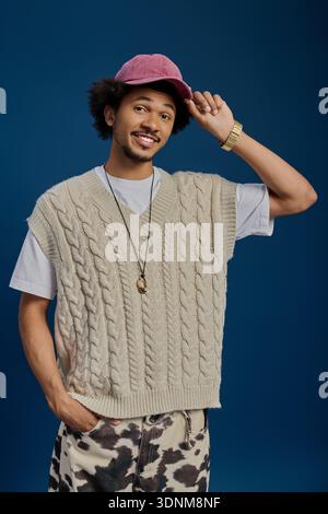Fröhlicher junger Mann trägt einen gemütlichen Pullover und eine Mütze, die seine charmante Persönlichkeit und Mode zum Ausdruck bringen. Stockfoto