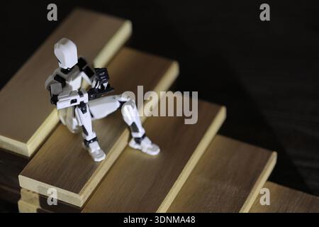 Eine ruhige Pause auf dem Weg nach oben. Die Figur sitzt nachdenklich auf Holztreppen, als ob sie eine kurze Pause einlegt und nachdenkt, bevor sie ihre Reise nach oben fortsetzt. Stockfoto