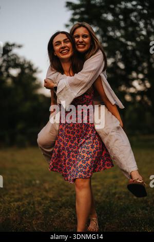 Zwei Frauen teilen sich einen fröhlichen Huckepack-Moment in einem sonnigen Park, in dem sie Freundschaft schließen Stockfoto