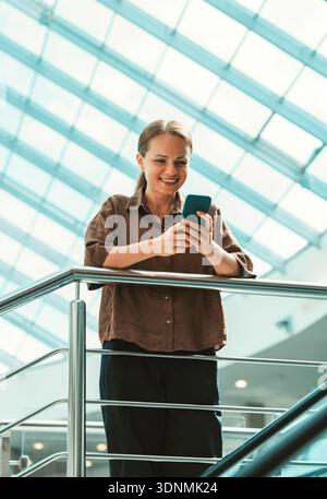 Junge Frau, die mit dem Smartphone im Internet surft, in einem hellen, modernen Innenraum Stockfoto