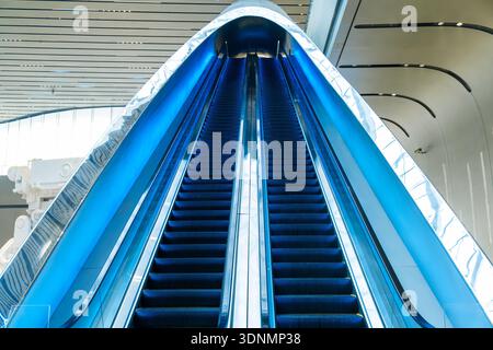 Moderne blaue Rolltreppen in einem futuristischen Gebäude mit geschwungener Architektur und glänzenden Oberflächen mit symmetrischer Perspektive in Chengdu City, China Stockfoto