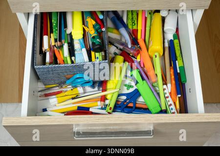 Unordentliche offene Schublade voller farbenfroher Schulpapiere und Bleistifte. Stockfoto
