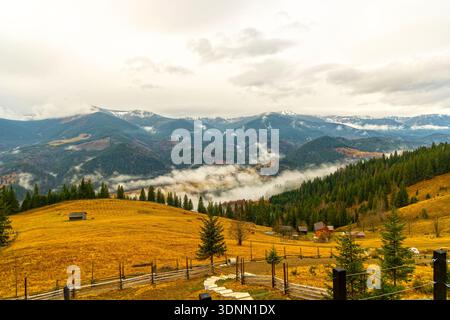 Bergdorf im Herbst mit nebeligen Hügeln. Malerischer Blick auf ein abgelegenes Bergdorf mit sanften Hügeln, farbenfrohen Herbstbäumen und tiefliegendem Nebel Stockfoto