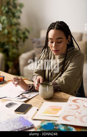 Eine junge afroamerikanische Frau genießt ihre Zeit in einem stilvollen Apartment, während sie Tee schlürft. Stockfoto