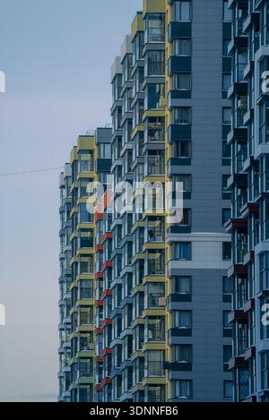 Städtischer Wohnhochhaus mit mehreren Fenstern, Balkonen und Designelementen für Außenfassaden vor hellem Himmel, die moderne Architektur und ein dichtes Stadtleben veranschaulichen Stockfoto