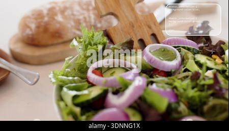 Weiße Schüssel mit frischem Grün auf dem Lichttisch, Holzgabel, Gurke und Tomatenhälften Stockfoto