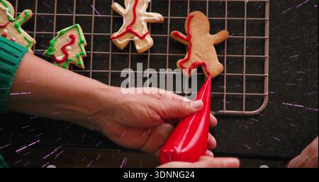 Grüne Hände schmücken rote Glasur aus rotem Backbeutel auf Lebkuchenkeksen zu Hause Stockfoto