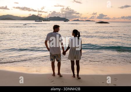 Ein paar Spaziergänge Hand in Hand entlang des unberührten Sandes von Anse Patates bei Sonnenuntergang. La Digue, Seychellen Stockfoto