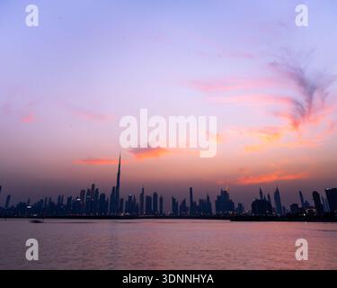 Blick auf die Skyline, die sich im Wasser unter einem sanften rosa und violetten Himmel in der Abenddämmerung spiegelt, Dubai, Vereinigte Arabische Emirate. Stockfoto