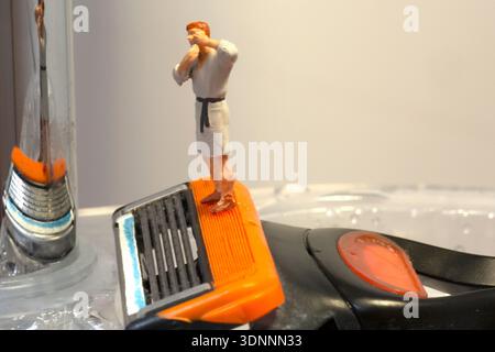 Miniaturfigur im Bademantel, stehend auf einem Rasierer in einer inszenierten Badezimmerszene. Stockfoto
