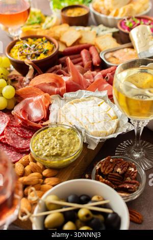 Versammelt um eine wunderschön gestaltete Wurstplatte gefüllt mit verschiedenen Käsesorten, köstlichen Würstchen, cremigem Hummus und frischen Trauben. Perfekt für kleine Treffen Stockfoto
