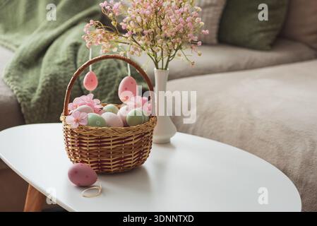 Osterkorb mit Ester-Eiern, Plüschhase und Frühlingsdekor auf weißem Tisch im Cozy Wohnzimmer Stockfoto