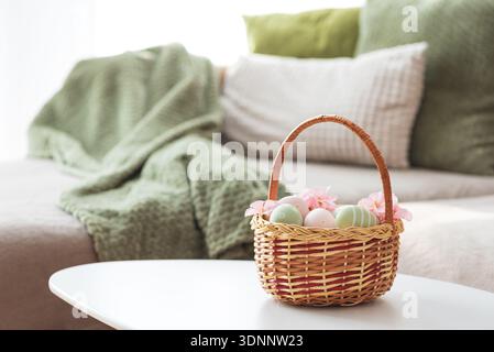 Osterkorb mit Ester-Eiern, Plüschhase und Frühlingsdekor auf weißem Tisch im Cozy Wohnzimmer Stockfoto