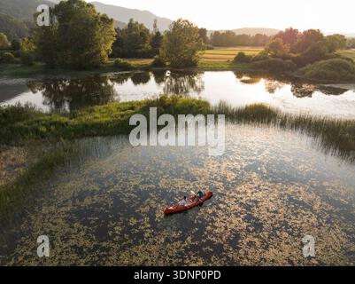 Paare Kajaks auf einem See bei Sonnenuntergang mit Bergen im Hintergrund und grünen Bäumen herum, genießen die gemeinsame Zeit in der Natur. Drohne aus der Luft Stockfoto