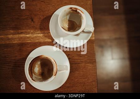 Zwei leere Cappuccino-Tassen mit Schaumstoffspuren ruhen nach dem Trinken auf einem Holztisch. Konzept von vollendetem Moment, gemeinsamer Zeit, Erinnerung und ruhigem Café Stockfoto
