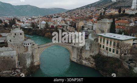 Blick aus der Vogelperspektive auf die historische Steinbrücke über den Neretva Fluss in Mostar mit der Architektur der Altstadt, türkisfarbenem Wasser und den umliegenden Bergen Stockfoto