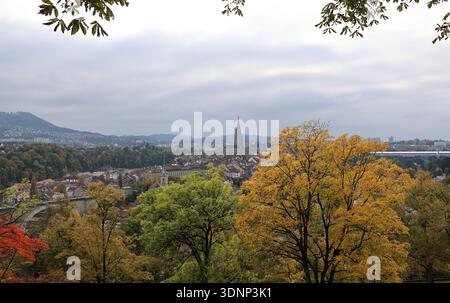 Bern, Schweiz – Blick auf die Skyline der Altstadt mit farbenfrohen Herbstbäumen und historischer Architektur unter bewölktem Himmel. Stockfoto
