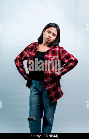 Ein Ganzkörperporträt einer stilvollen südostasiatischen Frau, die selbstbewusst mit Händen auf den Hüften posiert und ein rotes kariertes Hemd und Jeans trägt. Stockfoto