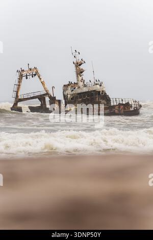 Ein verrostetes Schiffswrack liegt an Namibias Skeleton Coast vor turbulenten Wellen und spiegelt die raue Schönheit der Region und die Geschichte der Seefahrt wider Stockfoto
