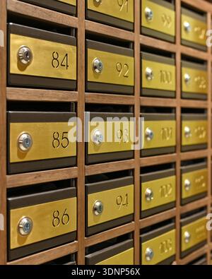 Nahaufnahme von Vintage-Messing-Briefkästen mit Kombinationsschlössern in einer Holzwand. Jede Box ist nummeriert und zeigt eine klassische und elegante Postaufbewahrung Stockfoto