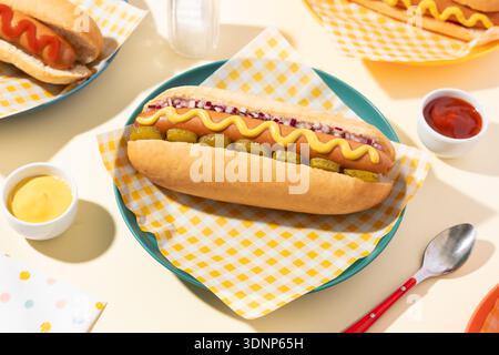 Ein köstlicher Hot Dog mit gelbem Senf, knusprigen Gurken und gehackten Zwiebeln. Serviert in einem Brötchen auf kariertem Papier, ist es ein Beispiel für einen klassischen fa Stockfoto