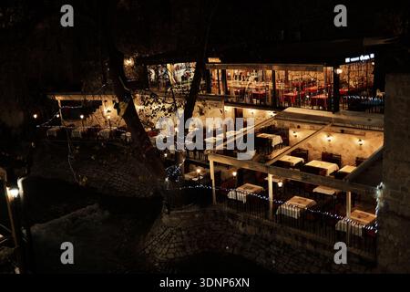 Abendblick auf eine gemütliche Restaurantterrasse mit warmen Lichtern und Gäste, die in einem historischen Gebäude in der Altstadt von Mostar speisen. Mostar, Bosnien und Herzegowina Stockfoto