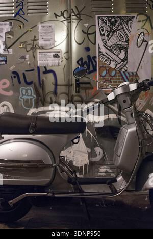 Vintage-Roller gegen die mit Graffiti bedeckte Stadtmauer bei Nacht Stockfoto