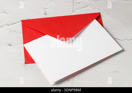 Roter Umschlag mit leerer Papierkarte Nahaufnahme auf hellem Betonsteinhintergrund. Mockup-Grußkarte mit Kopierraum Stockfoto