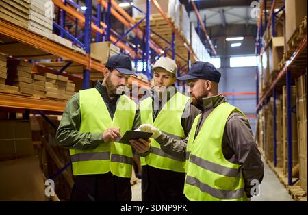 Logistikmitarbeiter prüfen Bestellungen auf Tablets im Lagerbestand zwischen Regalen Stockfoto
