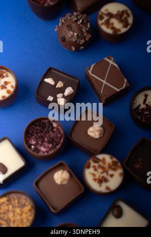 Close-up-Flachbild mit verschiedenen handwerklich hergestellten Schokoladentrüffeln und Pralinen, die auf einem lebhaften kobaltblauen Hintergrund angeordnet sind und Hochglanz-Ganache, Nuss-topp, hervorheben Stockfoto