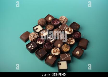 Verschiedene Gourmet-Schokoladen-Pralinen und Trüffel in einer lockeren Gruppe vor türkisfarbenem Studio-Hintergrund mit glänzenden Ganache, Nüssen und Früchten Stockfoto