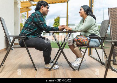 Glückliches Paar mit einer Beinprothese, die lächelt, während sie die Hände an einem Tisch im Freien hält Stockfoto
