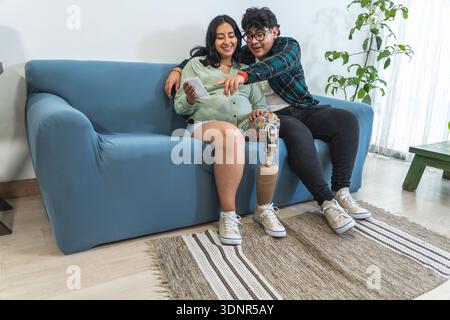 Schwangere Frau mit Beinprothetik und Partner, die auf dem Sofa sitzen, mit Ultraschallbild Stockfoto