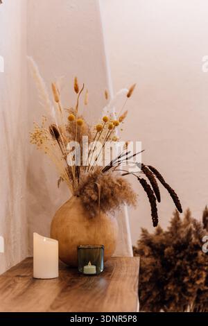Getrocknete Blumenstrauß in Keramikvase mit Kerze, warmes Boho-Dekor Stockfoto