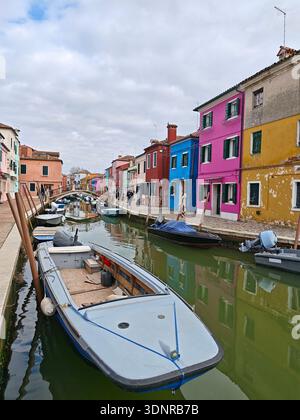 Kleine Boote, die entlang eines von bunten Häusern gesäumten Kanals in Burano nahe Venedig, Italien, im Februar 2026 vor Anker gebracht wurden. Stockfoto