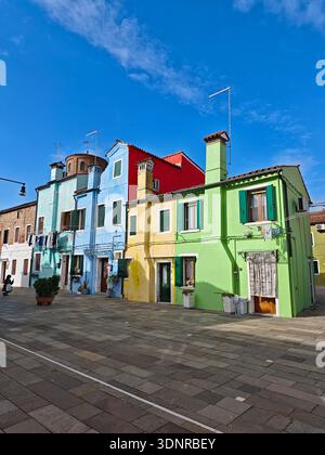 Burano, Venedig, Italien – Februar 2026: Bunte Pastellhäuser mit grünen Fensterläden säumen einen ruhigen Platz auf der Insel Burano in der Lagune von Venedig. Stockfoto