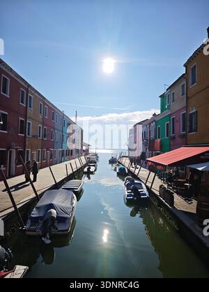 Farbenfrohe Kanalszene mit kleinen Booten und traditionellen Häusern unter hellem Sonnenlicht, Insel Burano, Lagune von Venedig, Italien. Stockfoto