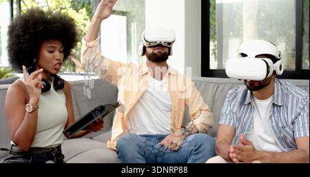 Testen von drei Erwachsenen mit weißen VR-Headsets auf grauem Sofa zu Hause, mit holografischer Benutzeroberfläche Stockfoto