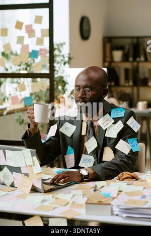 Schwarzer Mann, der mehrere Aufgaben mit Haftnotizen im modernen Büro verwaltet Stockfoto