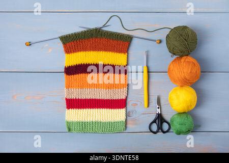 Arbeitstisch aus Holz mit Fadenkugeln und Stricknadeln, Schere, gestrickter Schal im Prozess, häkeln Stockfoto