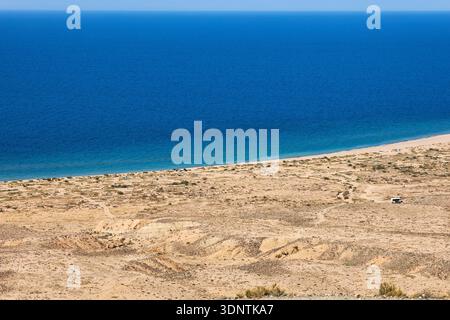 Blick aus der Vogelperspektive auf ein riesiges, ruhiges blaues Meer, das auf einen trockenen Sandstrand trifft. Broschüre für Reisen und Naturforschungen. Issyk Kul-See, Kirgisistan. Stockfoto